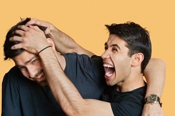 Young male friends playfighting over colored background